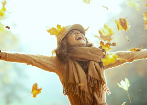 Woman in a fall setting outdoors tossing leaves into the air